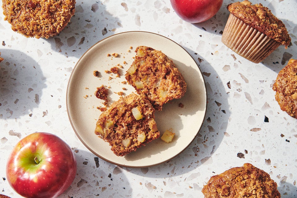 A freshly baked apple muffin split in half on a plate.
