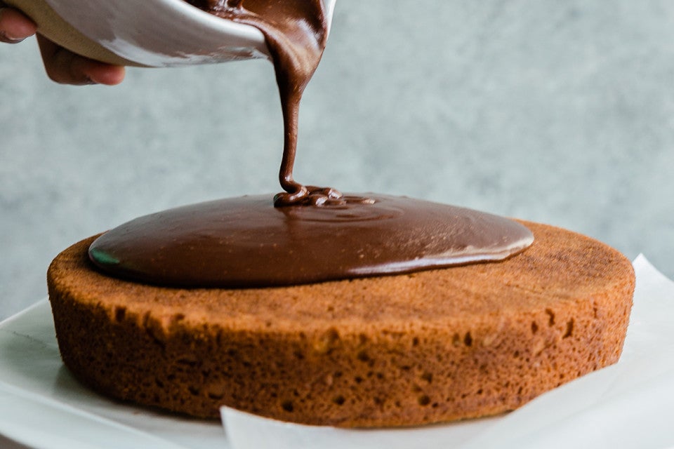 Yellow cake with fudge frosting being poured over it