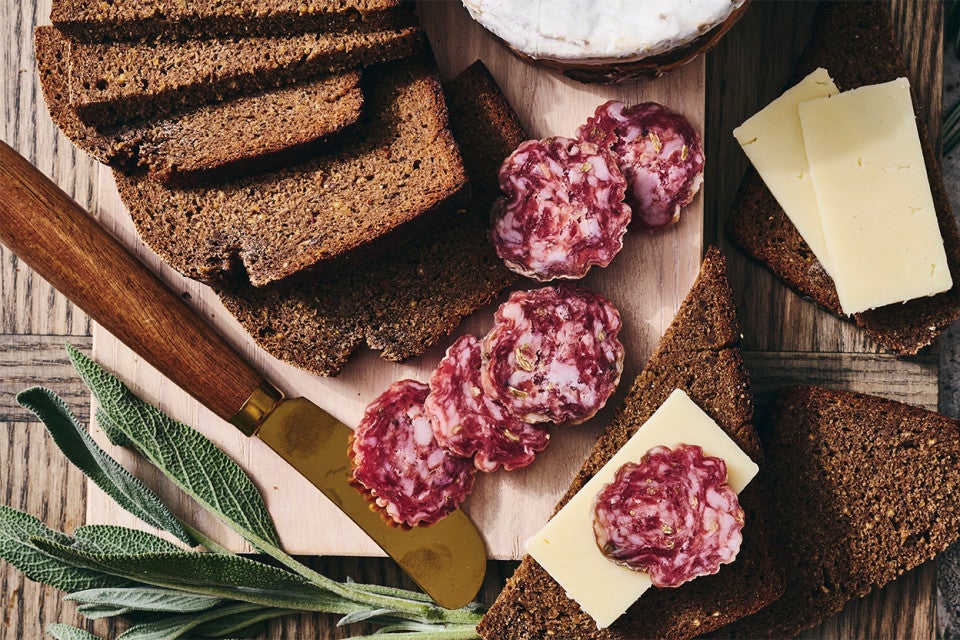 Classic Pumpernickel Bread sliced on a cutting board with meat and cheese