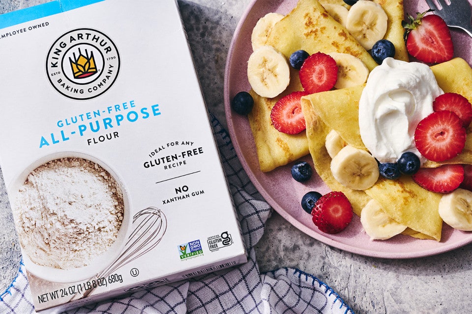 Gluten-Free Crêpes on a plate with berries and cream next to a box of gluten-free flour