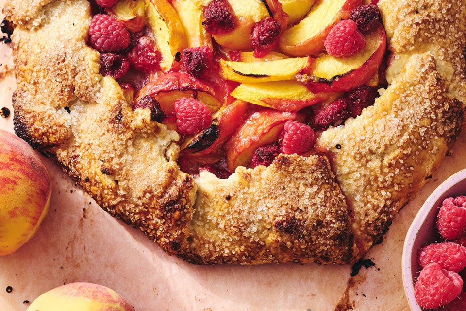 A close-up shot of a baked peach galette topped with raspberries
