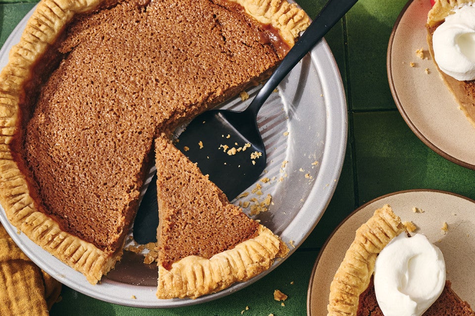 A slice of apple pie in the pie tin shown with a spatula under it and two slices on plates next to it.