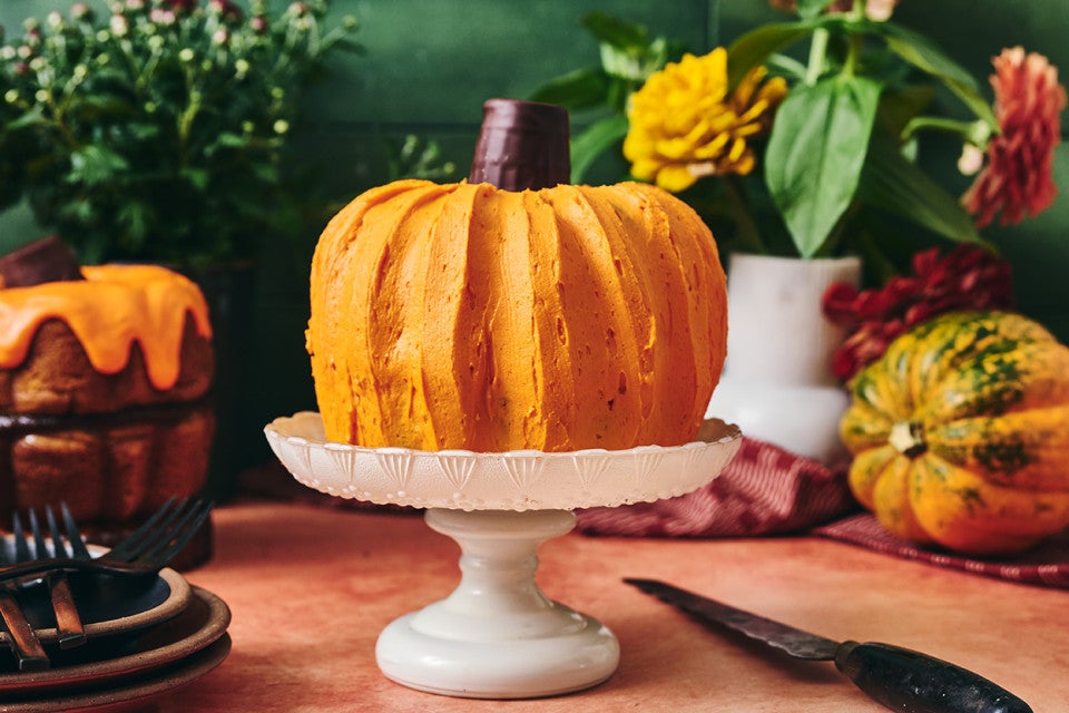 A bundt cake shown atop a white pedestal that looks very much like a pumpkin.