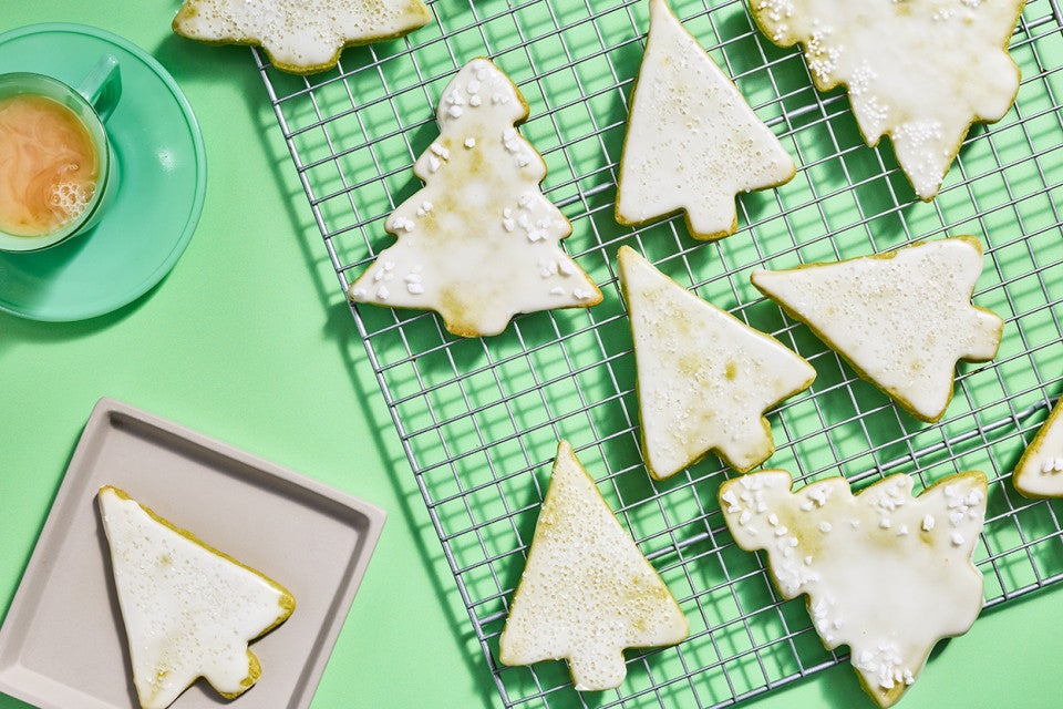 Christmas tree shaped cookies with a light white glaze spread out on a drying rack.