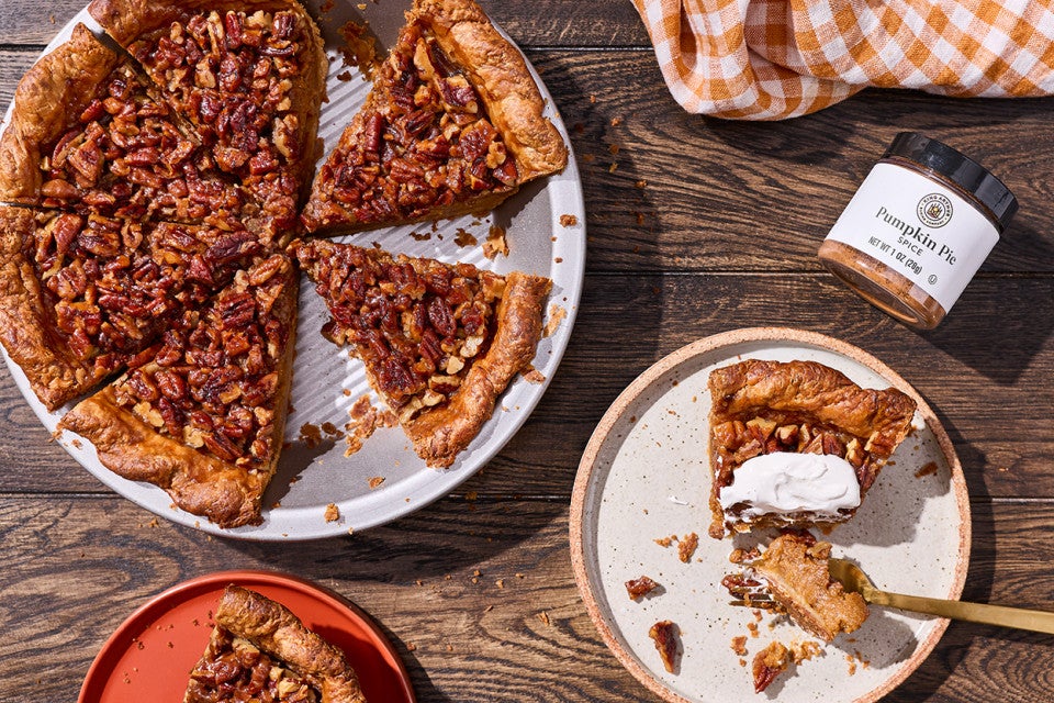 Looking at a rustic table with a pumpkin pecan pie slice and served on a plate, topped with whipped cream.