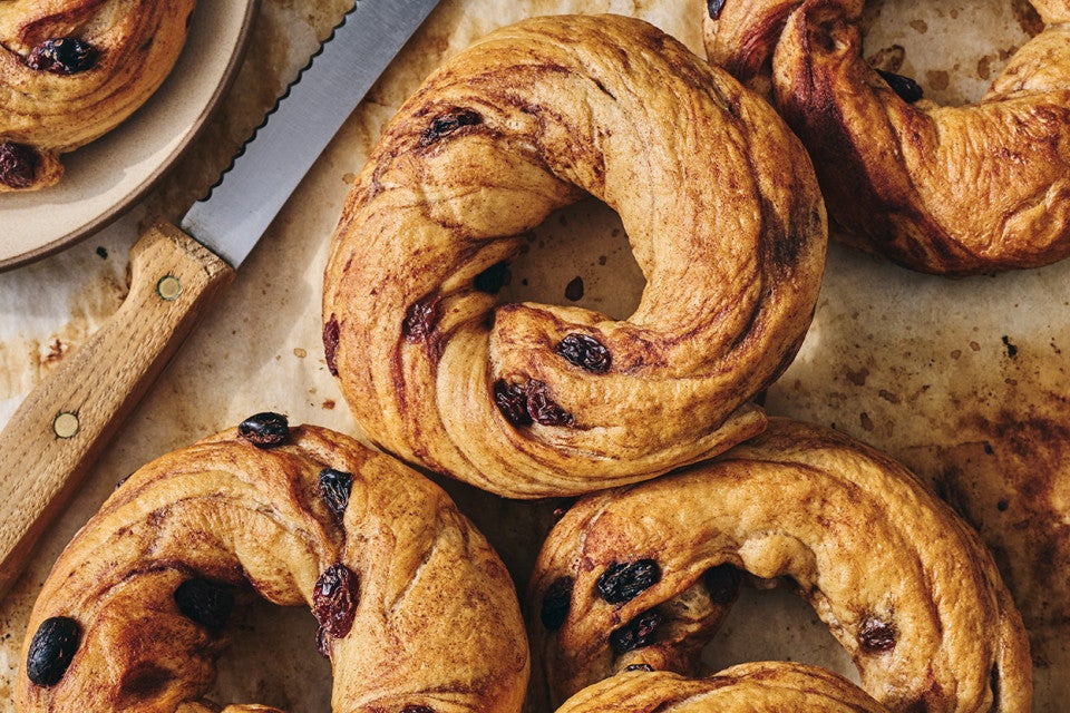 A handful of freshly baked Cinnamon Raisin Bagels on parchment paper seen from above.