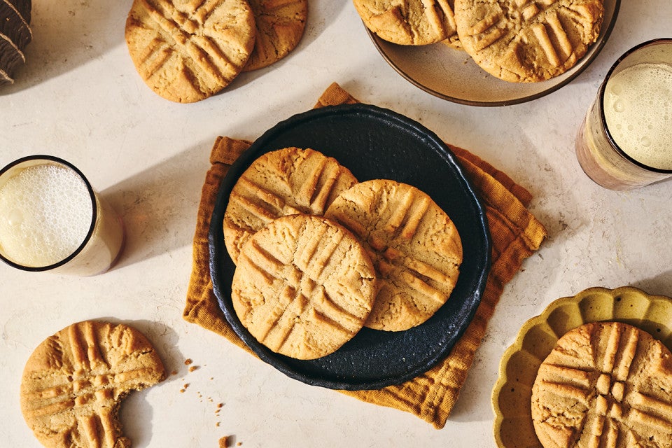 Classic Peanut Butter Cookies spread around a counter layout with some placed on a plate, others on decorative elements, and some on the counter itself. Glasses of milk are present too.