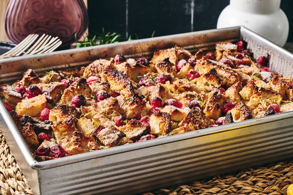 A photograph of the side of Cranberry-Rosemary Breakfast Pudding in a pan showing coarsely arranged and baked cranberries, bread, and roesmary.