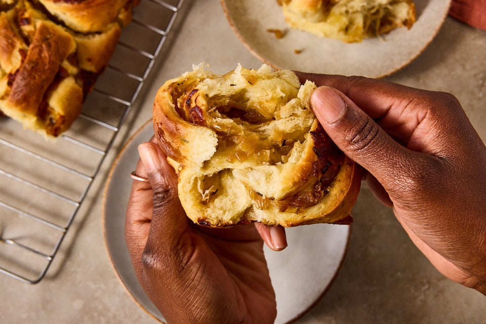 Hands pulling apart a French Onion Roll to show the structure and layers of dough and caramelized onions.