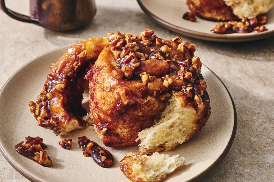Photograph of a dark brown sticky bun peeled apart showing with a sweet and perfectly baked interior.