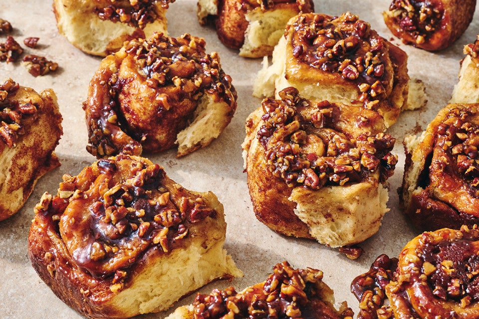 Multiple sticky buns separated on a counter top showing the golden interior and sticky glazed tops coated in nuts.