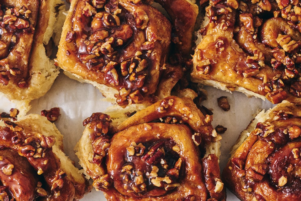 Overhead view of a tray of dark brown sticky buns fresh out of the oven and covered in nuts and glaze.