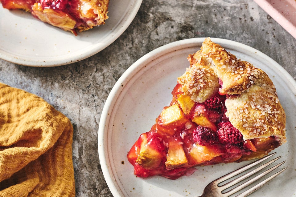 A slice of Rustic Raspberry-Peach Pie with a folded crust over the edge and vibrant fruit filling.