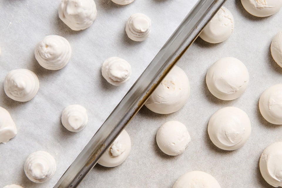 Swiss Meringue piped into round balls on sheet trays atop parchment paper ready for the oven.