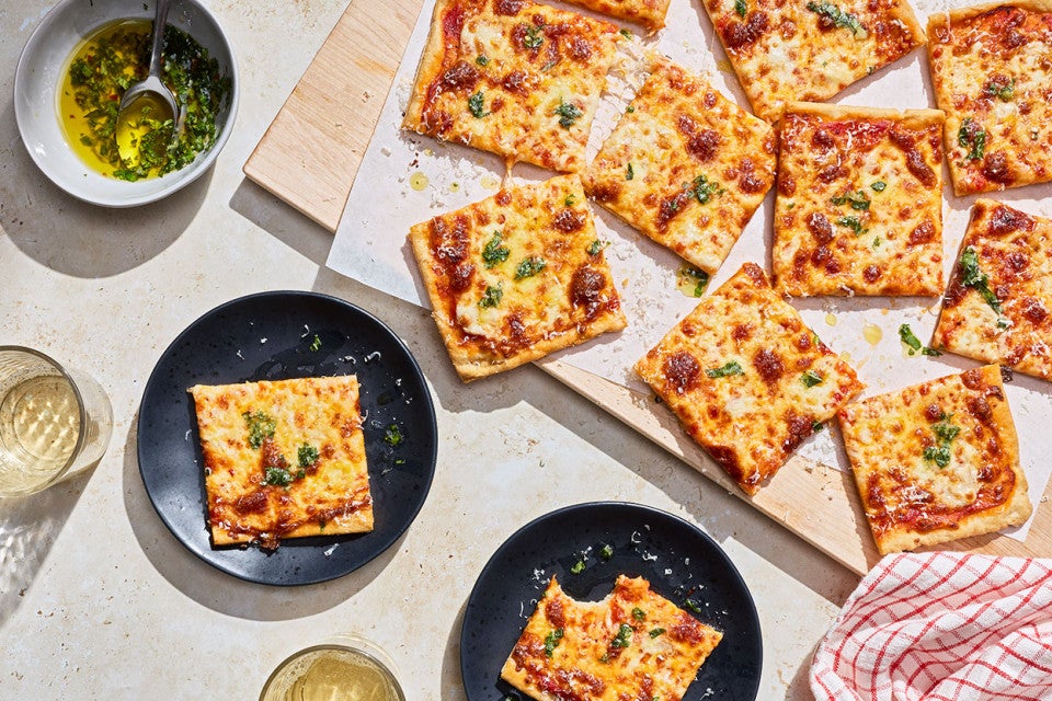Slices of Gluten-Free Sheet Pan Pizza seen from above and randomly arranged on a cutting board with other slices on plates.