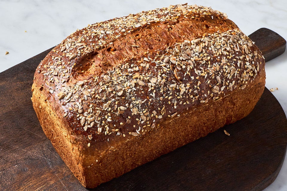 A loaf of Multigrain Protein Bread on a dark brown cutting board.