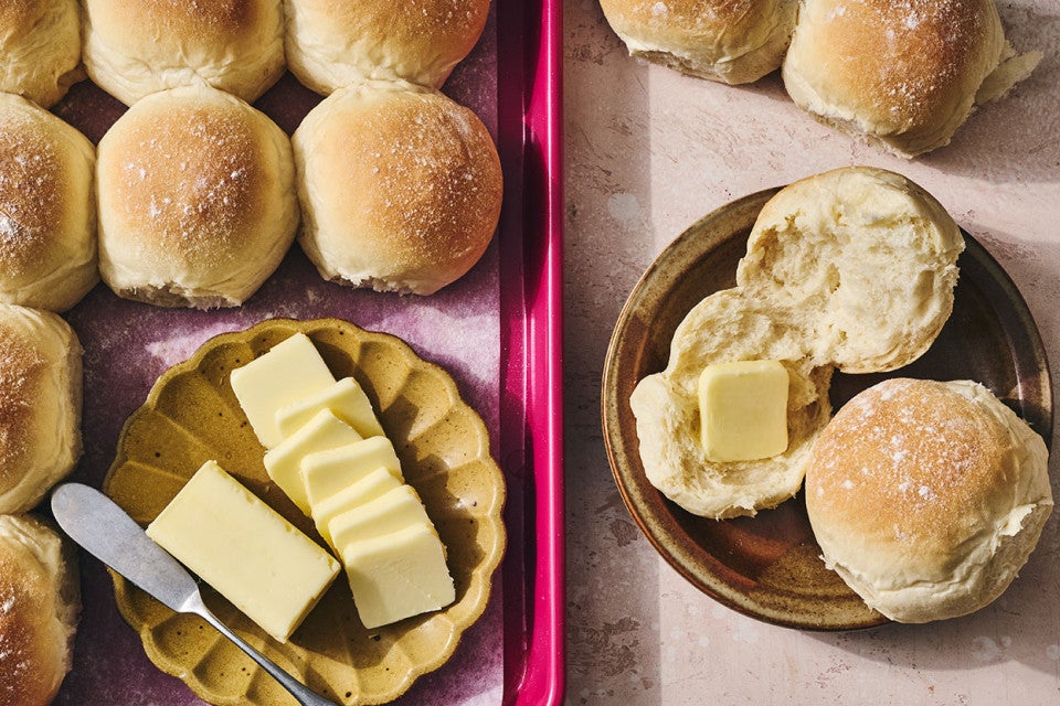Big-Batch Quick Dinner Rolls on a baking sheet and two on a plate with butter.