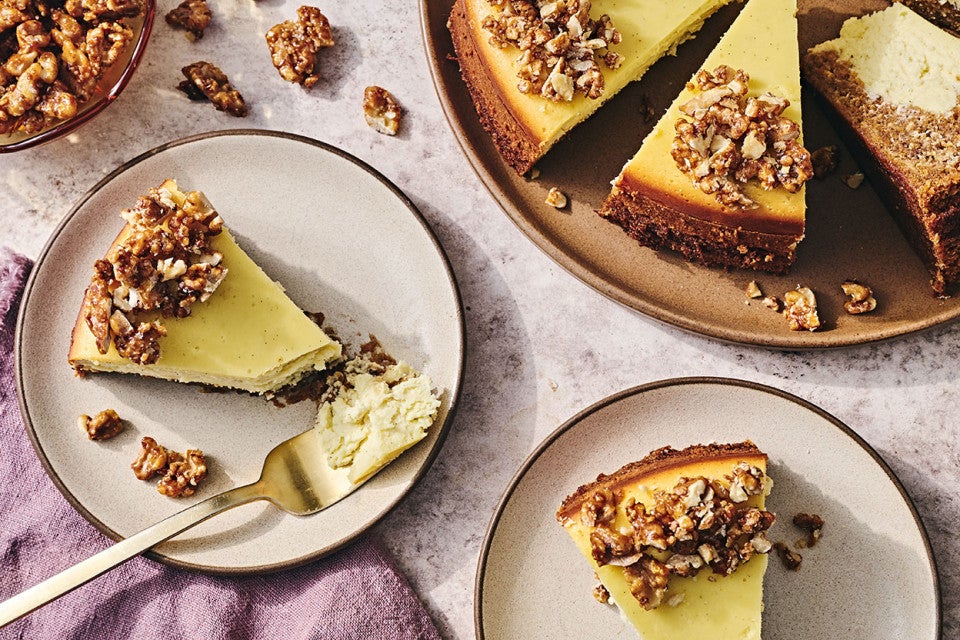 Carrot Cake Cheesecake on a table with slices on plates showing a golden cheesecake rimmed with nuts.