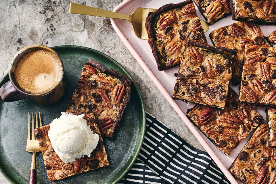 Two slices of Slab Chocolate Pecan Pie on a plate and one has vanilla ice cream on top.
