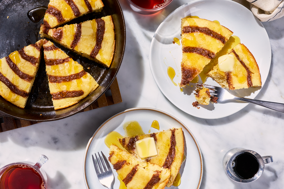 A Cinnamon Roll Skillet Pancake sliced up and shown in a cast iron skillet and also on plates.