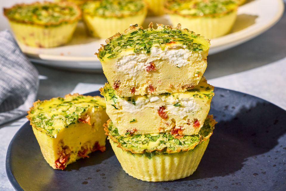 Egg Bites stacked on a plate with a cross-section showing a quiche like interior with greens, cottage cheese, and red pepper.