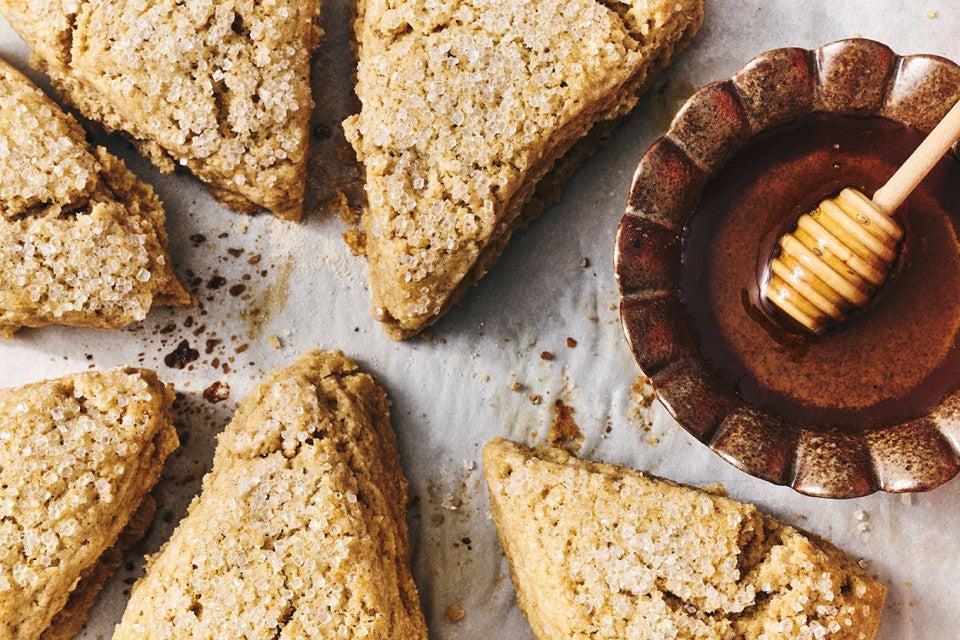 Looking down on Golden Wheat Scones with coarse sugar on top of them and a bowl of honey with a wooden honey wand.