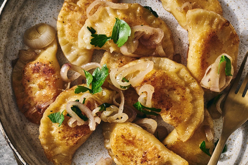 Homemade Pierogis on a plate with perfectly browned exteriors, garnished with herbs and onions.