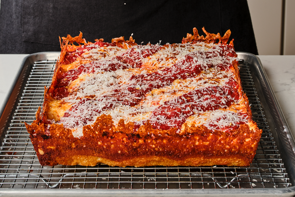 Detroit pizza on a baking rack showing the cooked pizza edges with crispy cheese and dough and a thick overall pizza.