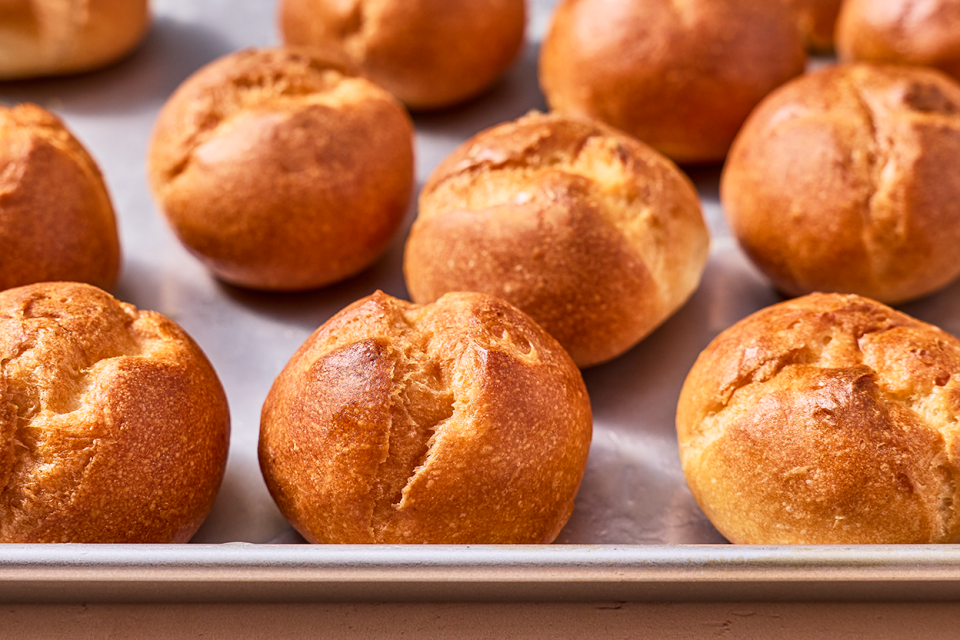 Freshly baked gluten-free rolls on a sheet tray with split tops and a deep golden crust.