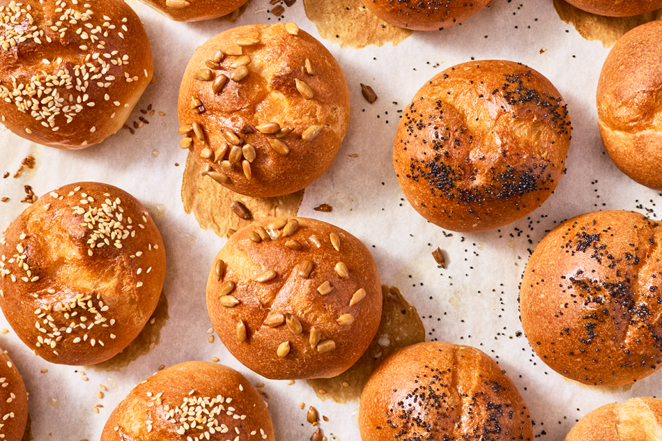 Freshly baked gluten-free rolls and buns on a sheet tray with split tops and a deep golden crust.
