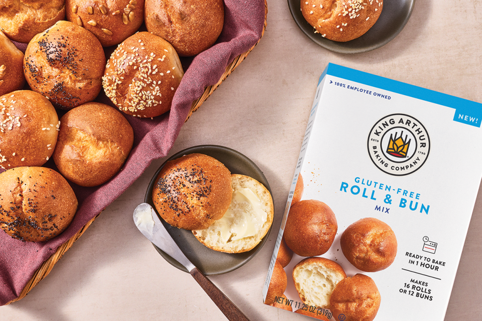 Guten-Free rolls and buns in a basked with another sliced and buttered on a plate and a box of King Arthur Baking's GF Roll & Bun Mix in the frame.