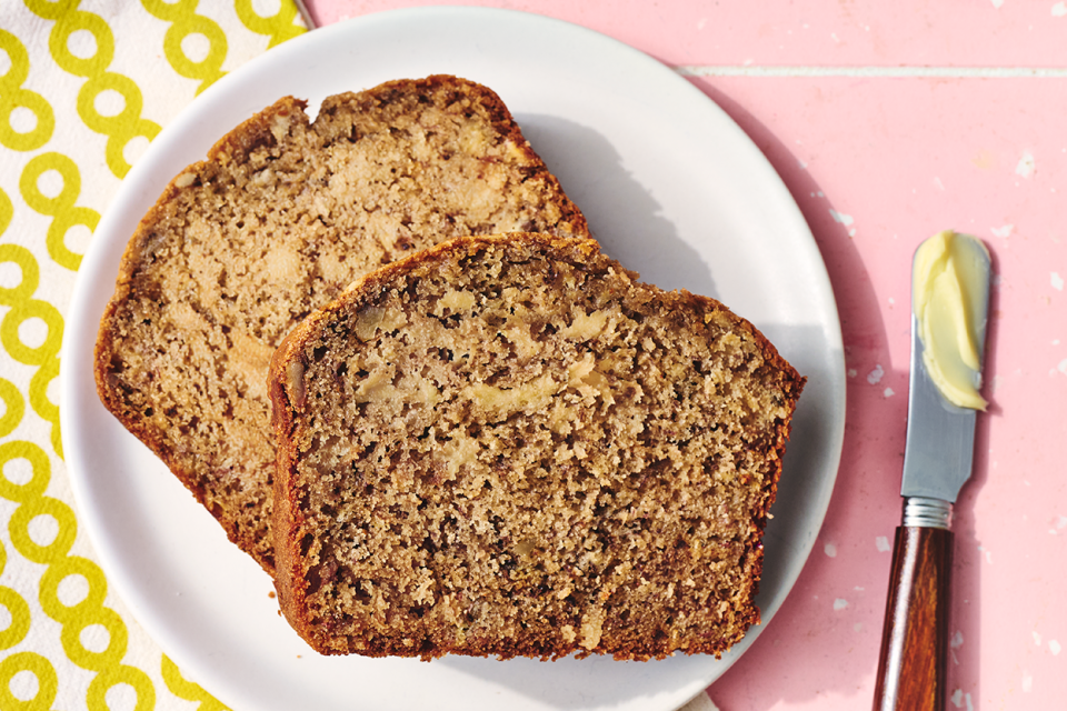 Two slices of sourdough banana bread on a plate with a buttered knife.