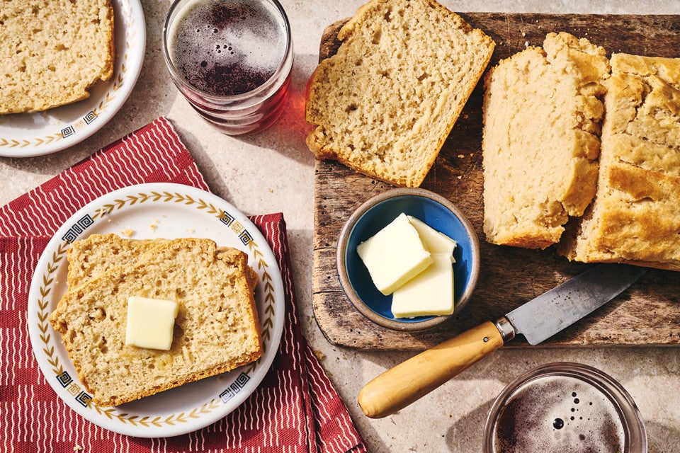 Sliced classic beer bread on a table with butter and a cutting board.