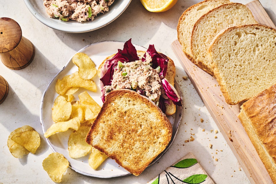 A sandwich, made with King Arthur's Classic Sandwich Bread, on a plate with chips and slices of bread on the table.