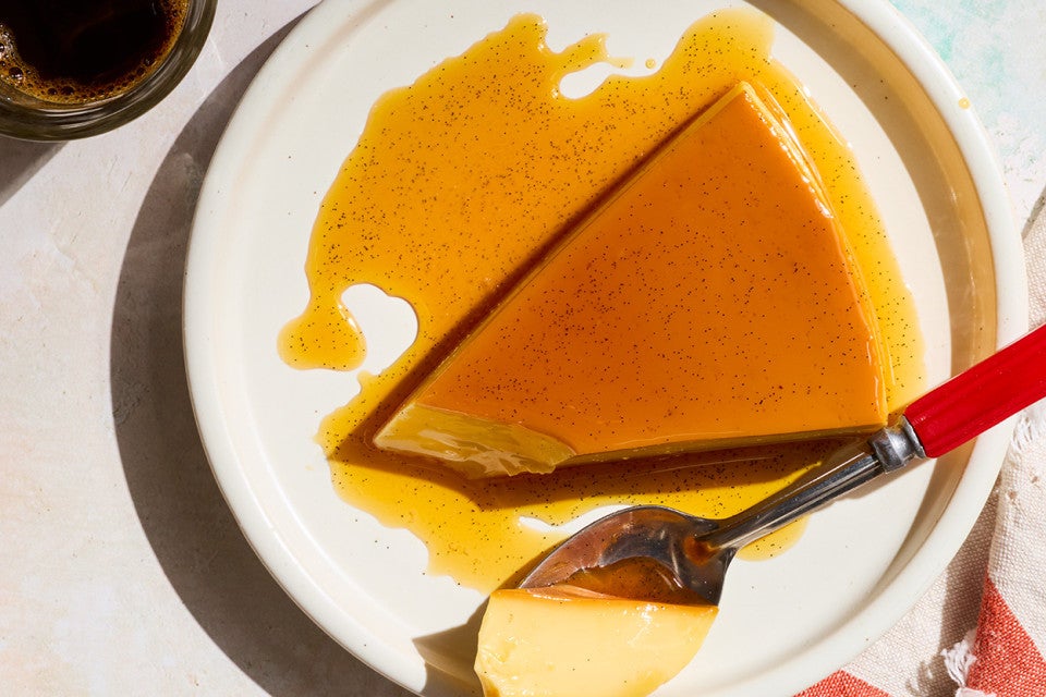 A slice of flan on a white plate with a bite on a spoon.