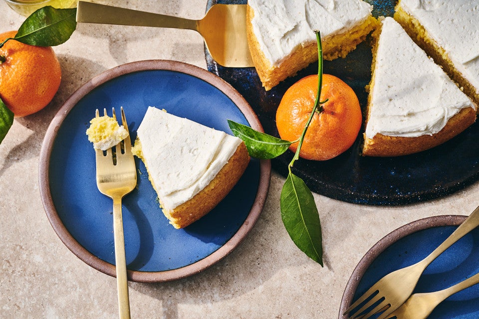 A slice of whole orange cake ona. blue plate with a bite on a fork.