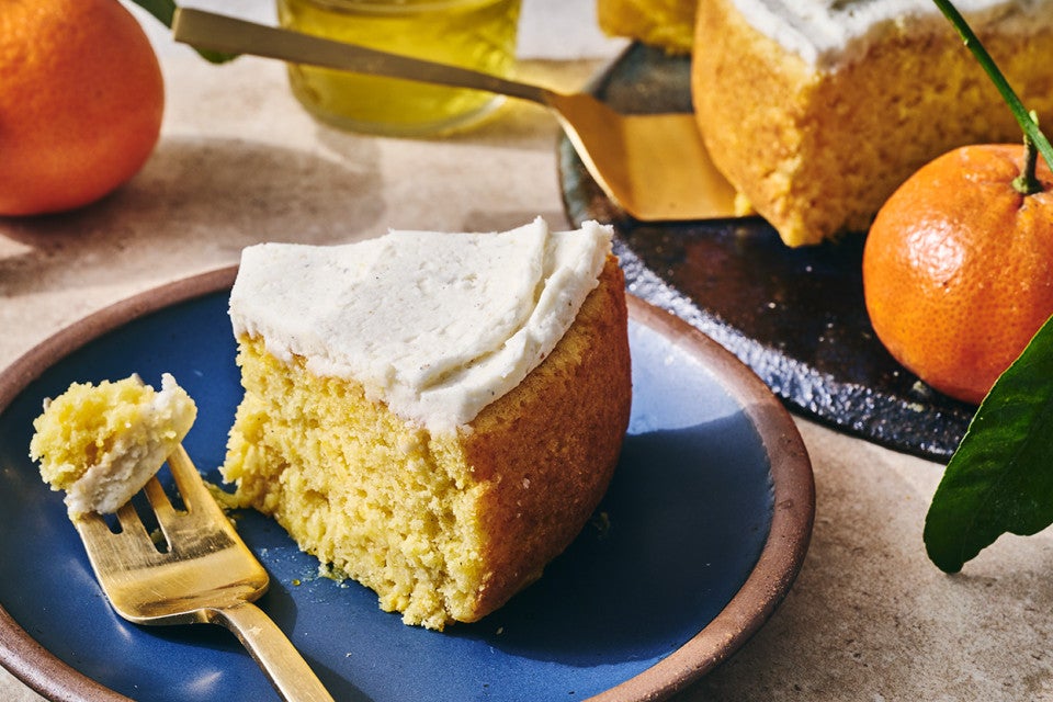 A slice of whole orange cake ona. blue plate with a bite on a fork.