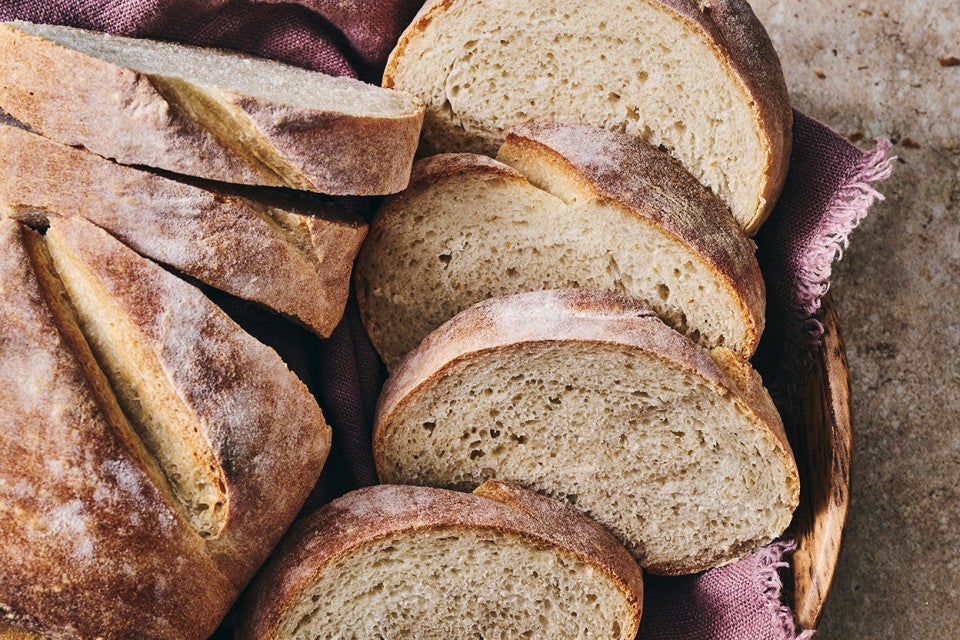 A rustic loaf of white bread in a basket with several slices.
