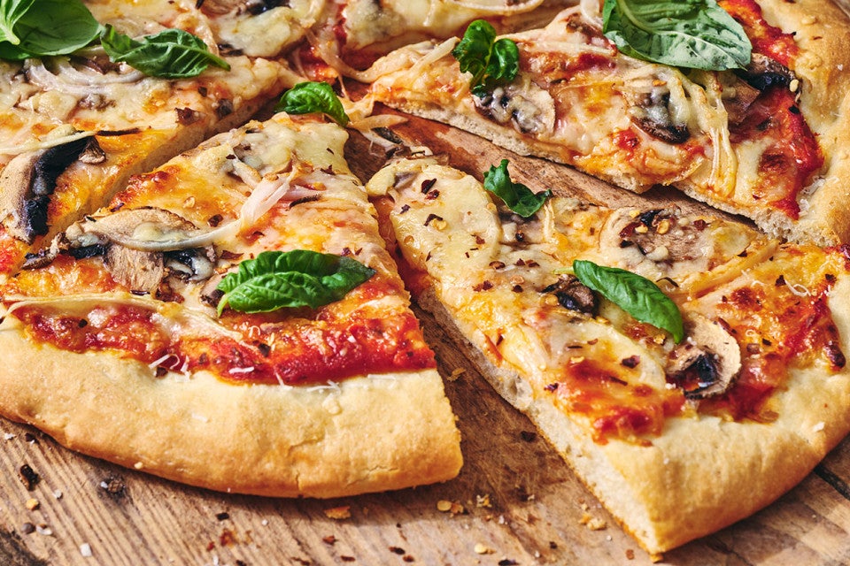 A slice of pizza slightly removed from a full pie