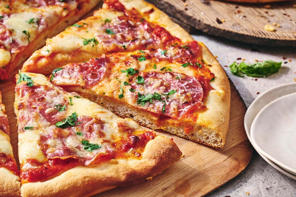 A slice of pizza slightly removed from a full pie