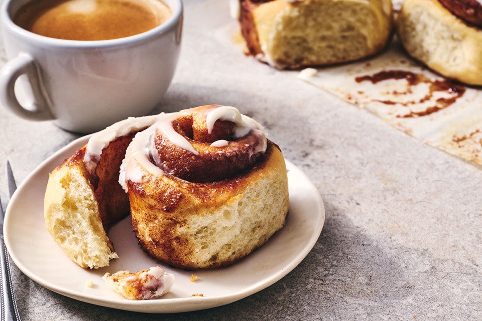 A Sourdough Cinnamon Roll on a plate accompanied by coffee - seen from the side.