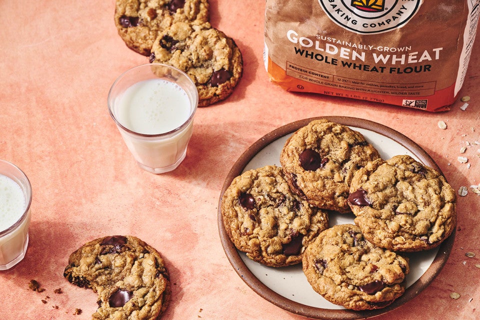 Whole Wheat Oatmeal Cookies on a plate with a glass of milk and a cookie with a bite taken out on a counter seen from above