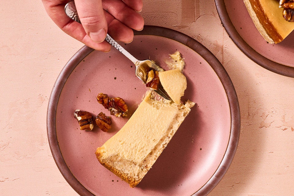 A person getting a bite of Maple Pecan Cheesecake from a slice on a pink plate