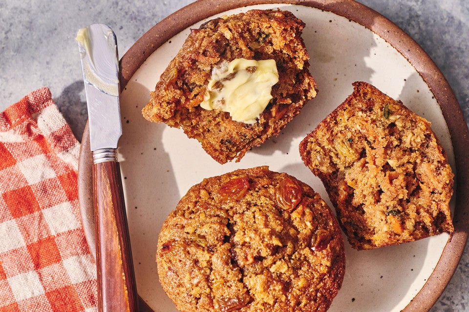 Morning Glory Muffins seen from above on a plate. One is split with butter on it.