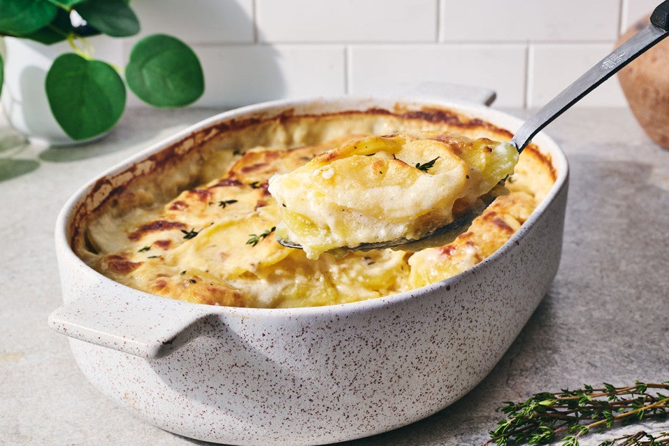 Scalloped potatoes being scooped out of a stoneware pan with a spoon