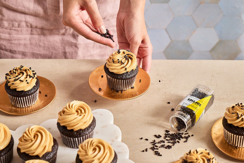 Adding sprinkles to the top of Chocolate Cupcakes with Whipped Caramel Frosting