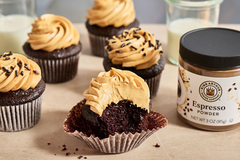 Chocolate Cupcakes with Whipped Caramel Frosting seen from the side with a jar of espresso powder from King Arthur Baking