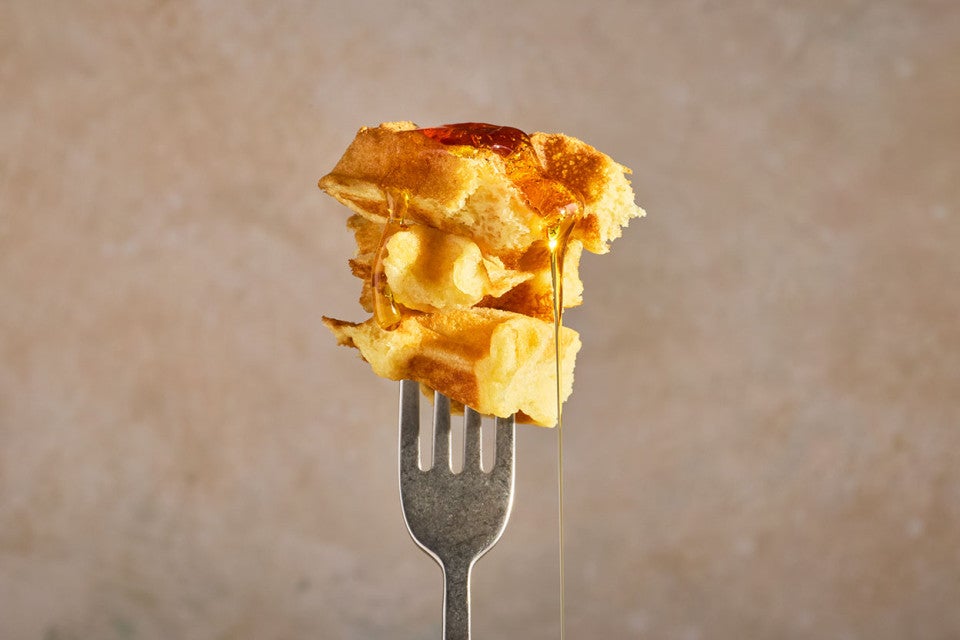 A fork with a bite of buttermilk waffles on it and syrup dripping down.
