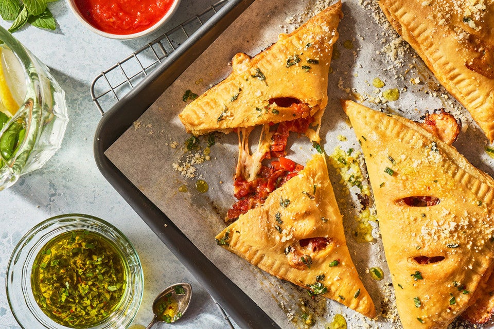 Flaky Puff Crust Pizza Turnovers on a baking sheet with herbs seen from above