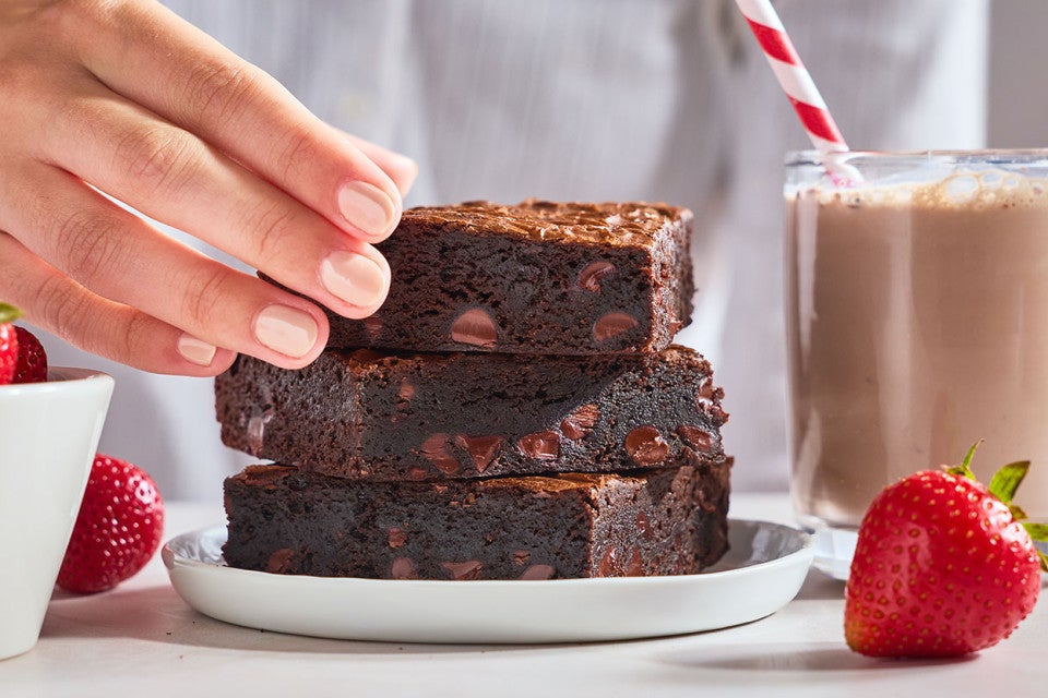 Fudge Brownies stacked on a plate with someone picking up the top one and strawberries in the foreground.